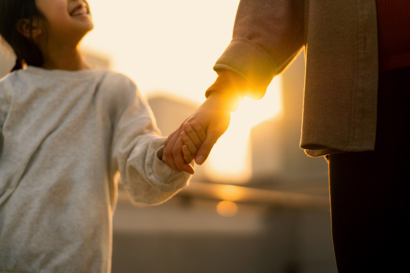 Barn og voksen holder hender i solnedgangen – et symbol på trygghet og tillit.